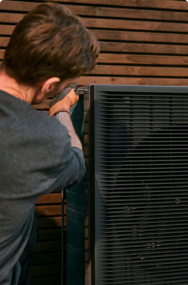 An engineer fitting an outdoor air source heat pump unit against a slatted wooden wall
