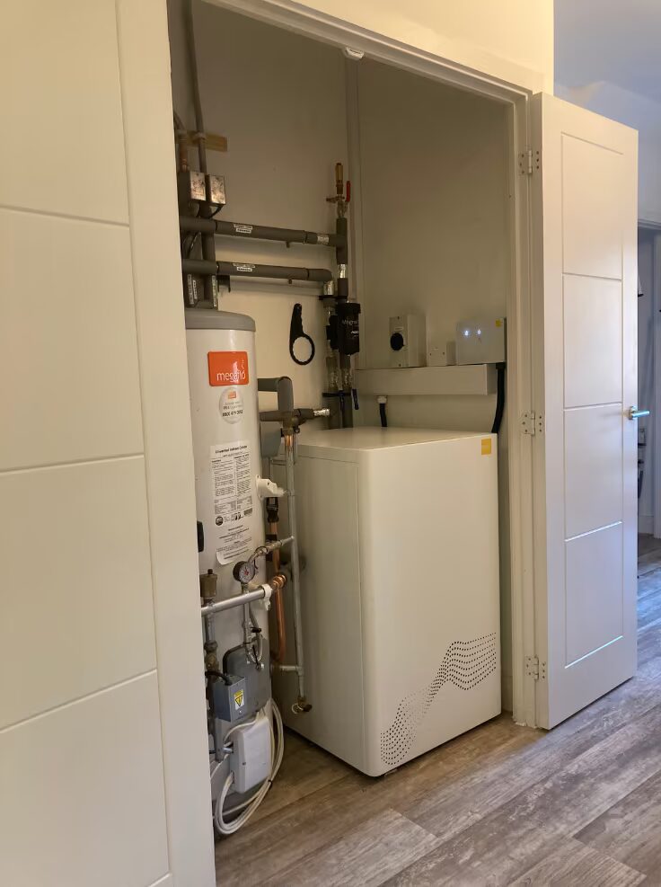 A heat pump unit and hot water cylinder with pipework installed inside a household airing cupboard