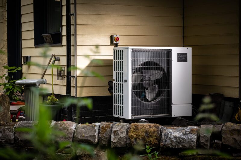 An air source heat pump unit installed outside a house beside a stone wall