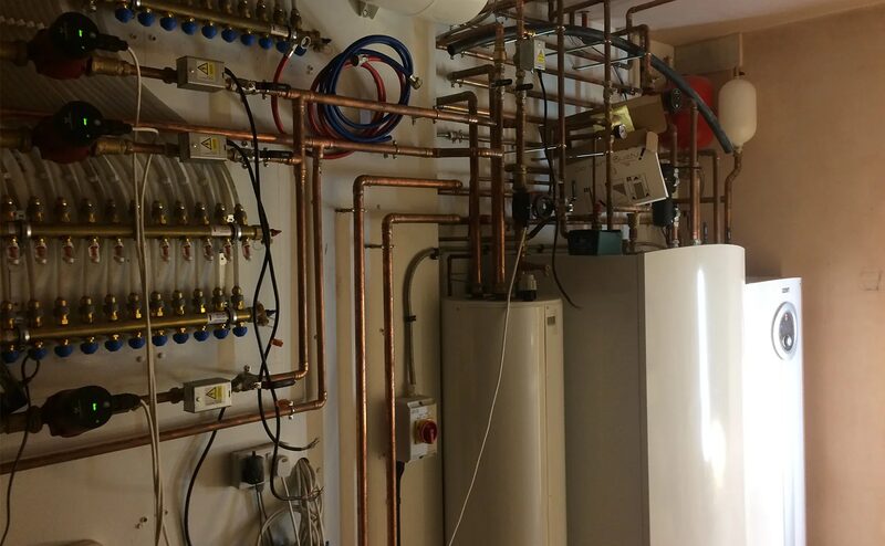 A plant room with copper pipework, manifolds and cylinders for an installed ground source heat pump system