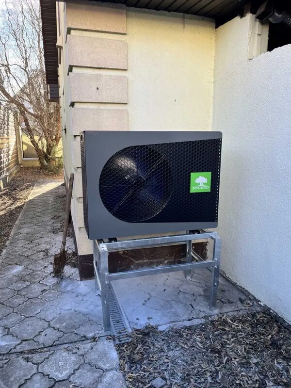 A Mycond air source heat pump outdoor unit installed on a metal stand beside a house wall