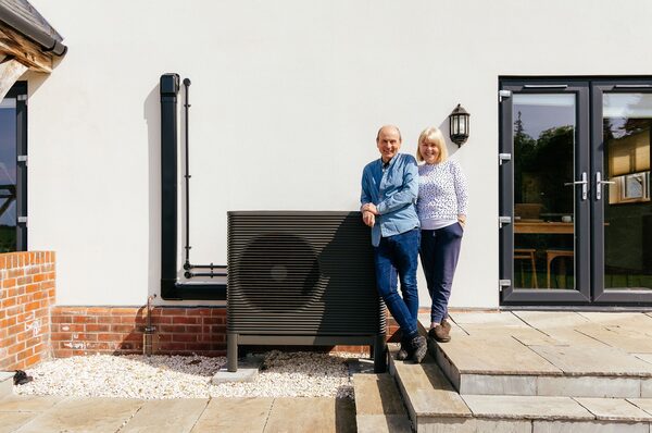A couple standing beside an air source heat pump installed outside their house