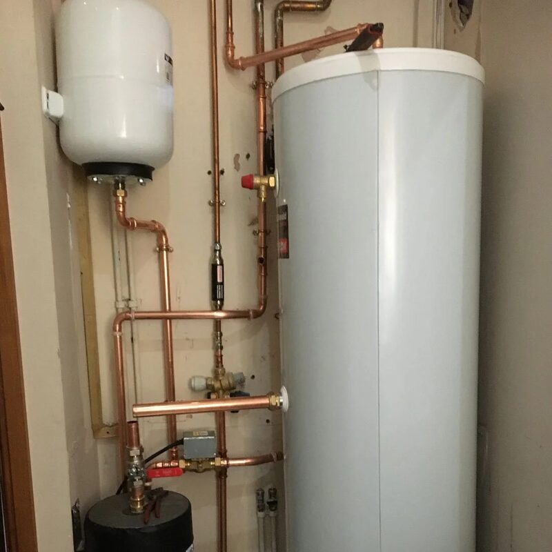 A large white hot water cylinder with copper pipework, expansion vessel and valves installed in a home airing cupboard
