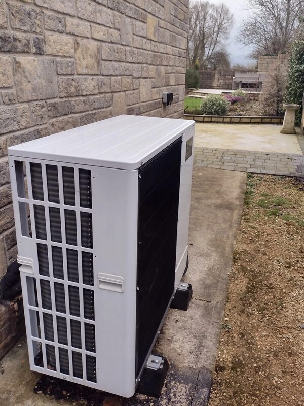 An air source heat pump unit installed outside a stone house next to a paved garden path