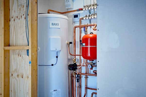 A white Baxi hot water cylinder installed in a plant cupboard with copper pipework, a red expansion vessel and manifold