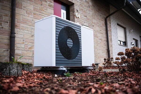 An air source heat pump unit installed outside a brick house beside the front door