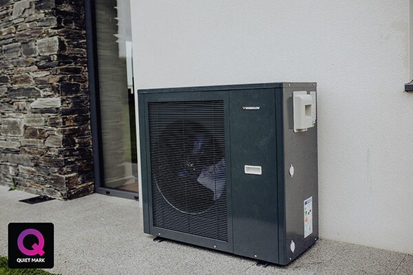 A dark grey air source heat pump unit installed outside a house wall next to a glass door