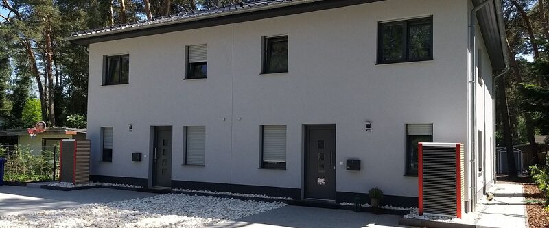 A modern semi-detached house with two heat pump outdoor units mounted on the exterior walls