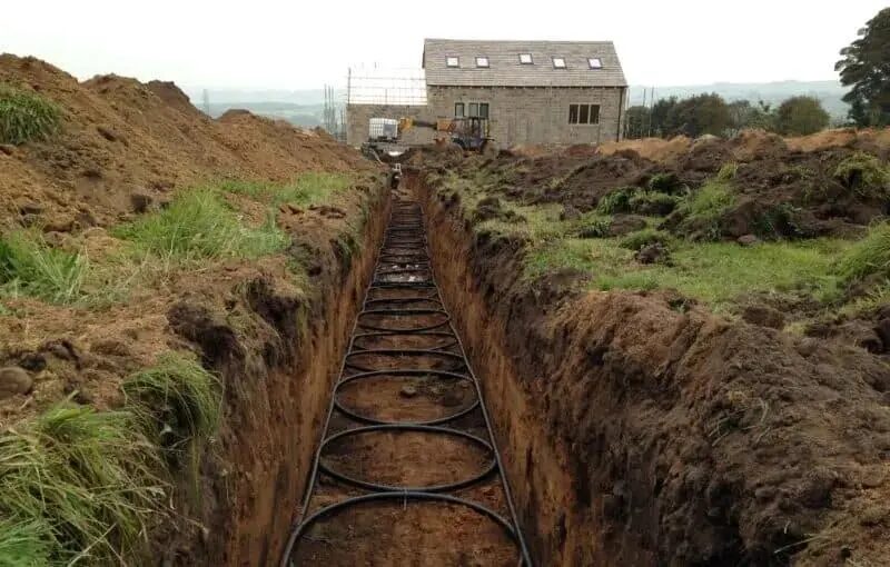 A slinky ground loop for a ground source heat pump being installed in a trench near a new-build house