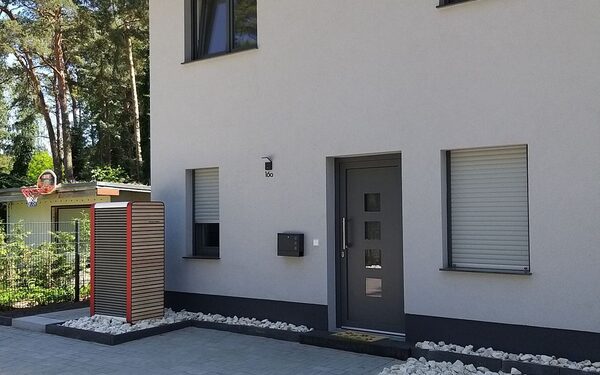 An outdoor air-source heat pump unit in a timber-clad casing beside the entrance of a modern grey semi-detached house