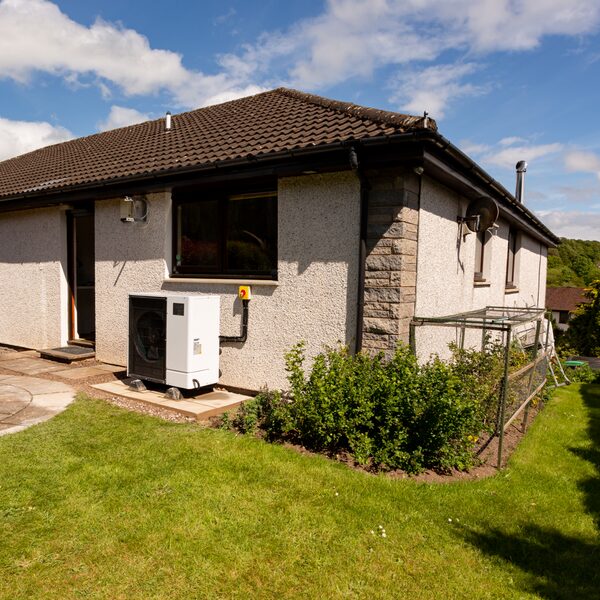 An air source heat pump unit installed on a concrete pad outside a rendered bungalow with a garden lawn