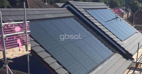 In-roof solar panels integrated into the slate roof of a new-build house under construction, with scaffolding at the side