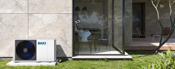 A white Baxi air source heat pump unit installed on a concrete pad outside a modern house with large glass doors