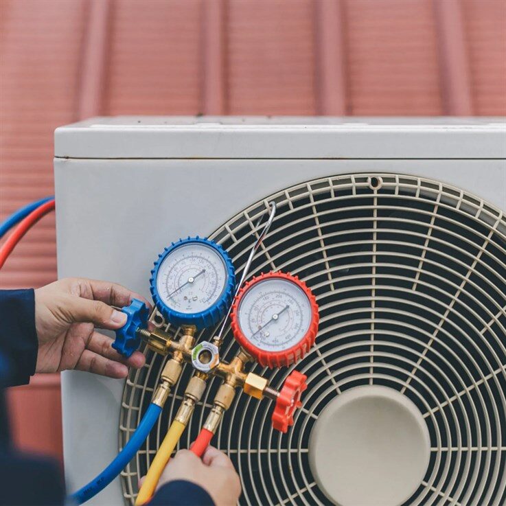 A technician using manifold pressure gauges to service an outdoor air conditioning / heat pump condenser unit