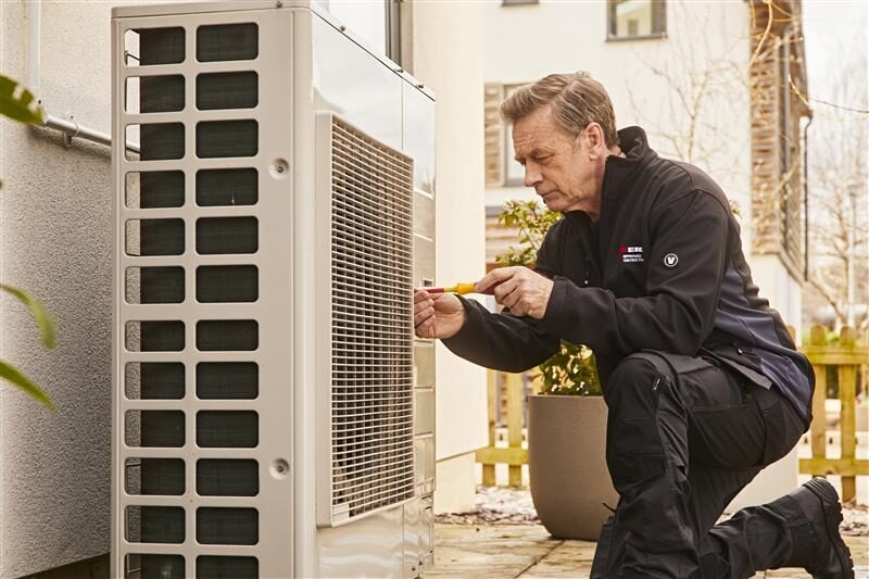 A technician in branded workwear servicing an outdoor air source heat pump unit outside a house