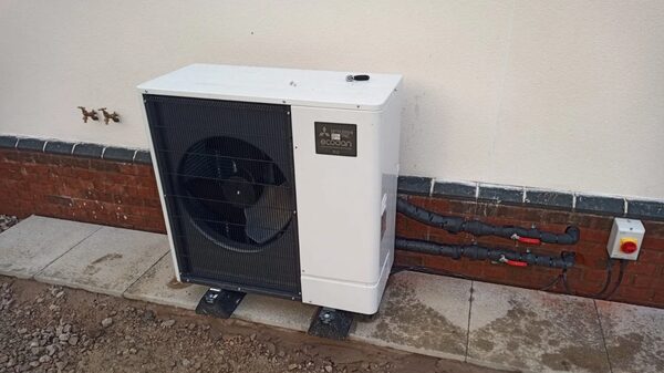 An air source heat pump unit installed outside a house against a brick and rendered wall with insulated pipework