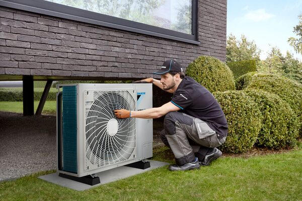 A Daikin engineer in branded uniform servicing an outdoor air source heat pump unit outside a modern house
