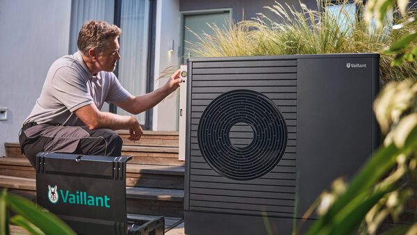 A technician kneeling beside an installed Vaillant air source heat pump outside a house, working on the unit with a Vaillant toolbox nearby
