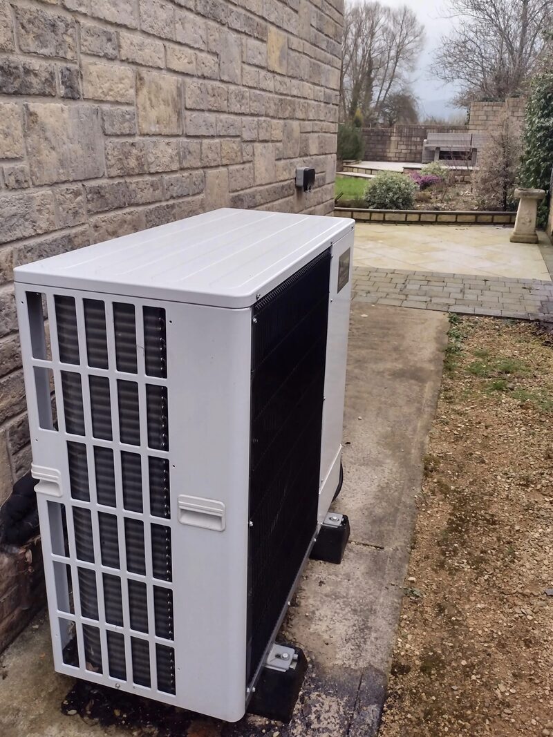 An air source heat pump unit installed outside a stone house next to a paved garden path