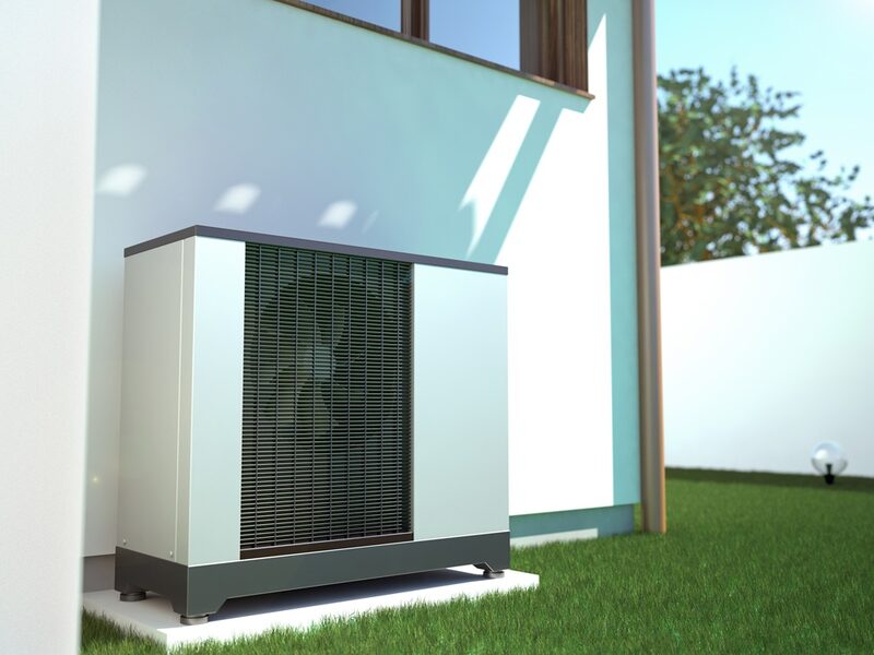 An air source heat pump unit installed on a concrete pad outside a house wall on a lawn