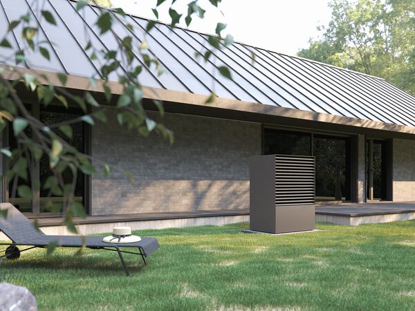 An air source heat pump unit installed on the lawn outside a modern single-storey house with a metal roof