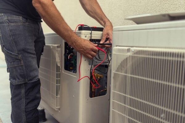 A technician wiring an outdoor air source heat pump unit outside a building