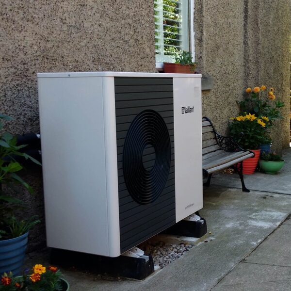 A Vaillant air source heat pump unit installed outside a house beside a bench and potted plants