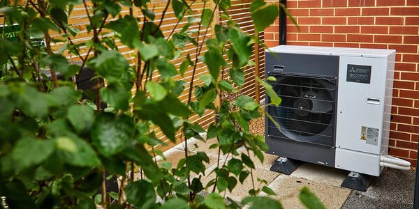 A Mitsubishi Ecodan air source heat pump unit installed outside against a brick wall, partly hidden by garden foliage