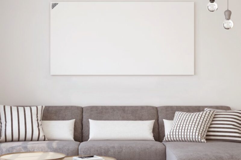 A white infrared heating panel mounted on a wall above a grey sofa in a living room