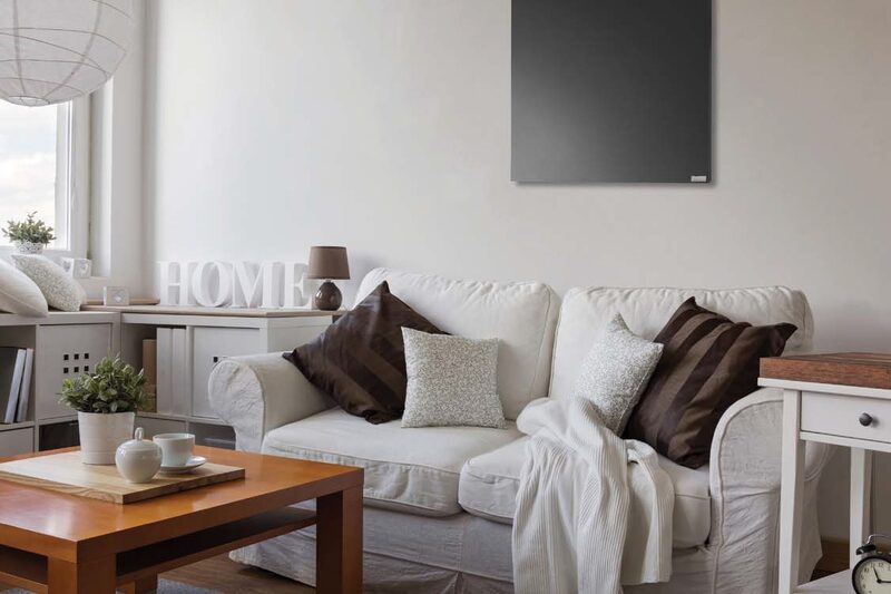 A grey infrared heating panel mounted on the wall of a bright living room with a white sofa