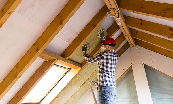 A man in a red cap and mask fitting mineral wool insulation between the rafters of a loft conversion