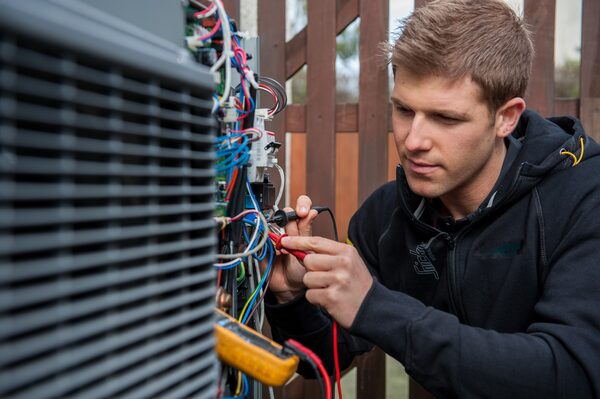 A technician using a multimeter to test the wiring of an outdoor air source heat pump unit