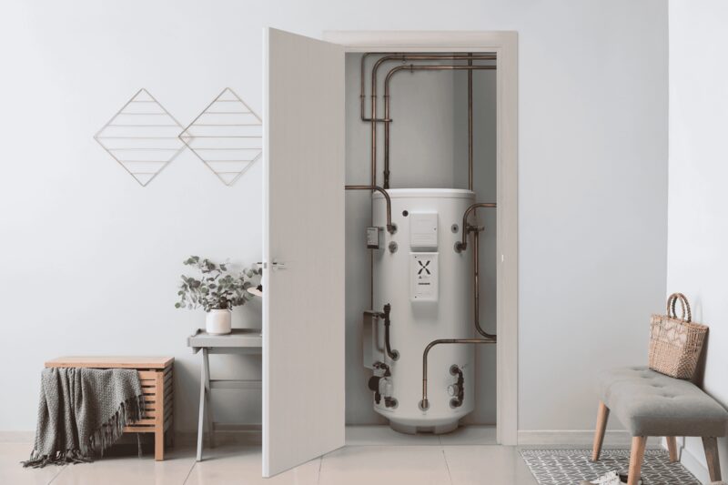 A Mixergy hot water cylinder installed in an airing cupboard behind an open door, with copper pipework