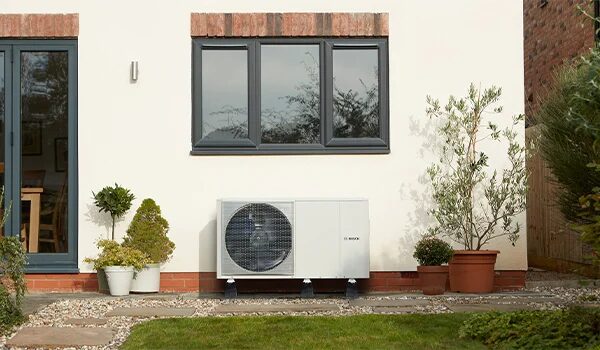 A Bosch air source heat pump unit installed on the exterior wall of a house beside a window and potted plants