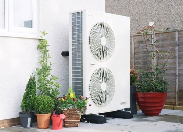 A Grant Aerona air source heat pump installed outside a house wall beside potted plants