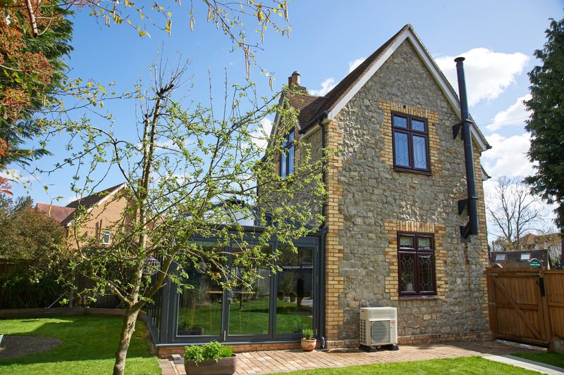 A stone house with an air source heat pump unit installed on the exterior wall beside a conservatory