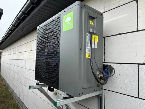 A Mycond air source heat pump outdoor unit mounted on a bracket against the white block wall of a house