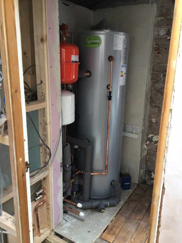 A hot water cylinder with expansion vessel and copper pipework installed in a small plant cupboard during a heat pump retrofit