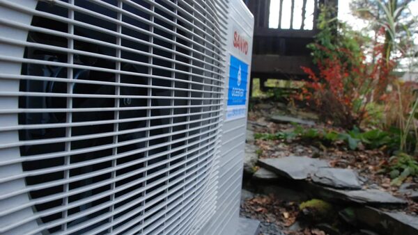 A Sanyo air source heat pump outdoor unit installed in a garden beside slate steps