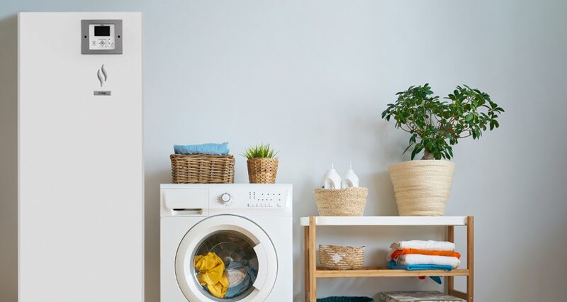 A white Hitachi Yutaki air-to-water heat pump cylinder installed in a utility room next to a washing machine and shelving with plants and towels