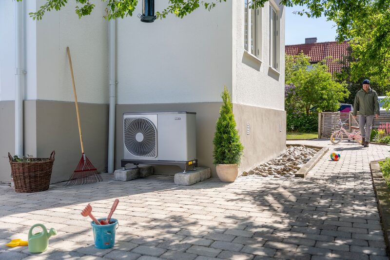 An outdoor air source heat pump unit installed on the side of a house next to a paved garden path