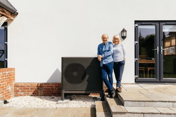 A couple standing beside an Aira air source heat pump installed outside their house