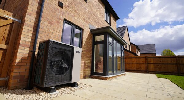 An air source heat pump unit installed on the gravel beside a brick house's patio