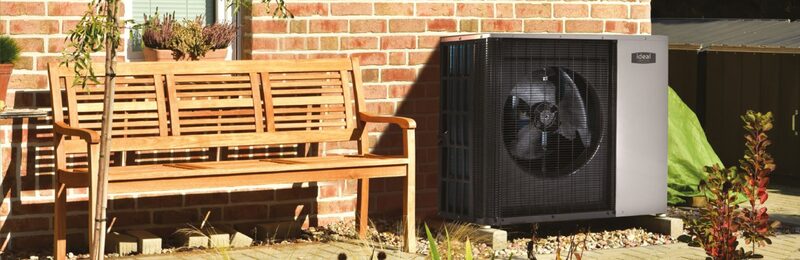 An Ideal Logic Air air source heat pump installed outside a brick house next to a wooden garden bench