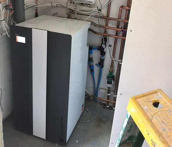 A Kensa Evo ground source heat pump unit installed indoors next to copper pipework and valves