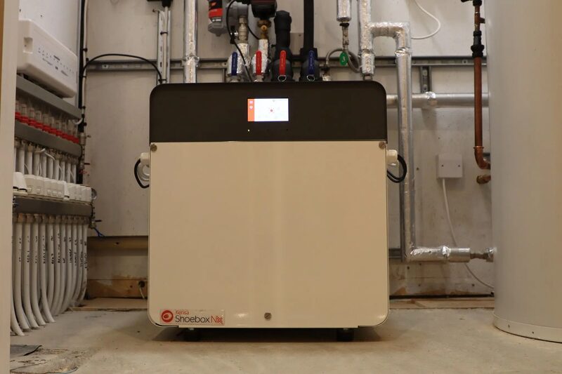 A Kensa Shoebox NX ground source heat pump installed in a plant room with pipework, manifolds and a hot water cylinder