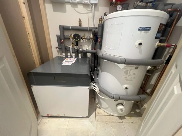 A ground source heat pump unit and hot water cylinder with pipework installed in a home utility cupboard
