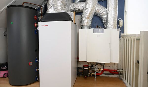 An installed all-in-one heat pump unit with a hot water cylinder and insulated ducting in a home utility space