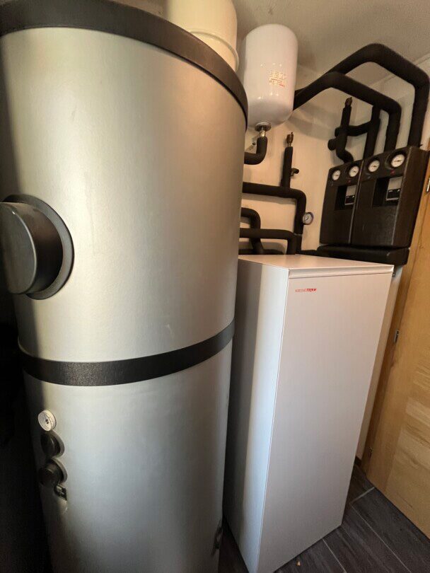 A Kronoterm heat pump indoor unit installed next to a large hot water cylinder and pipework in a utility space
