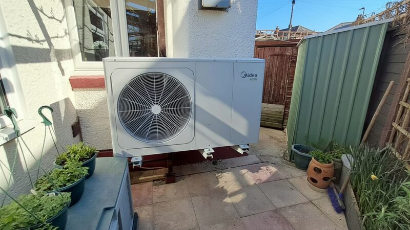 A Midea air source heat pump outdoor unit installed on a wall beside a house patio